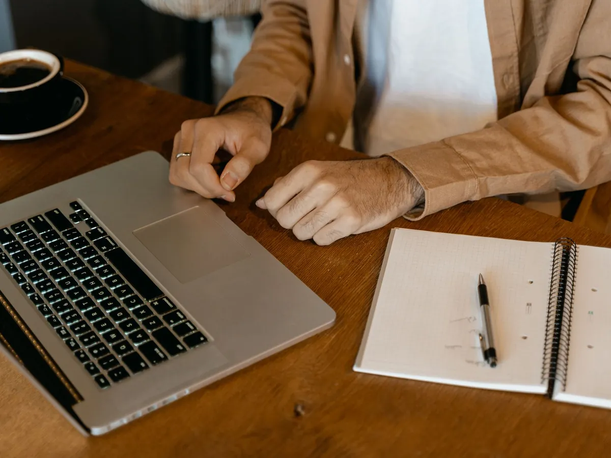 Gros plan d'un homme travaillant avec un ordinateur portable et un carnet sur un bureau en bois