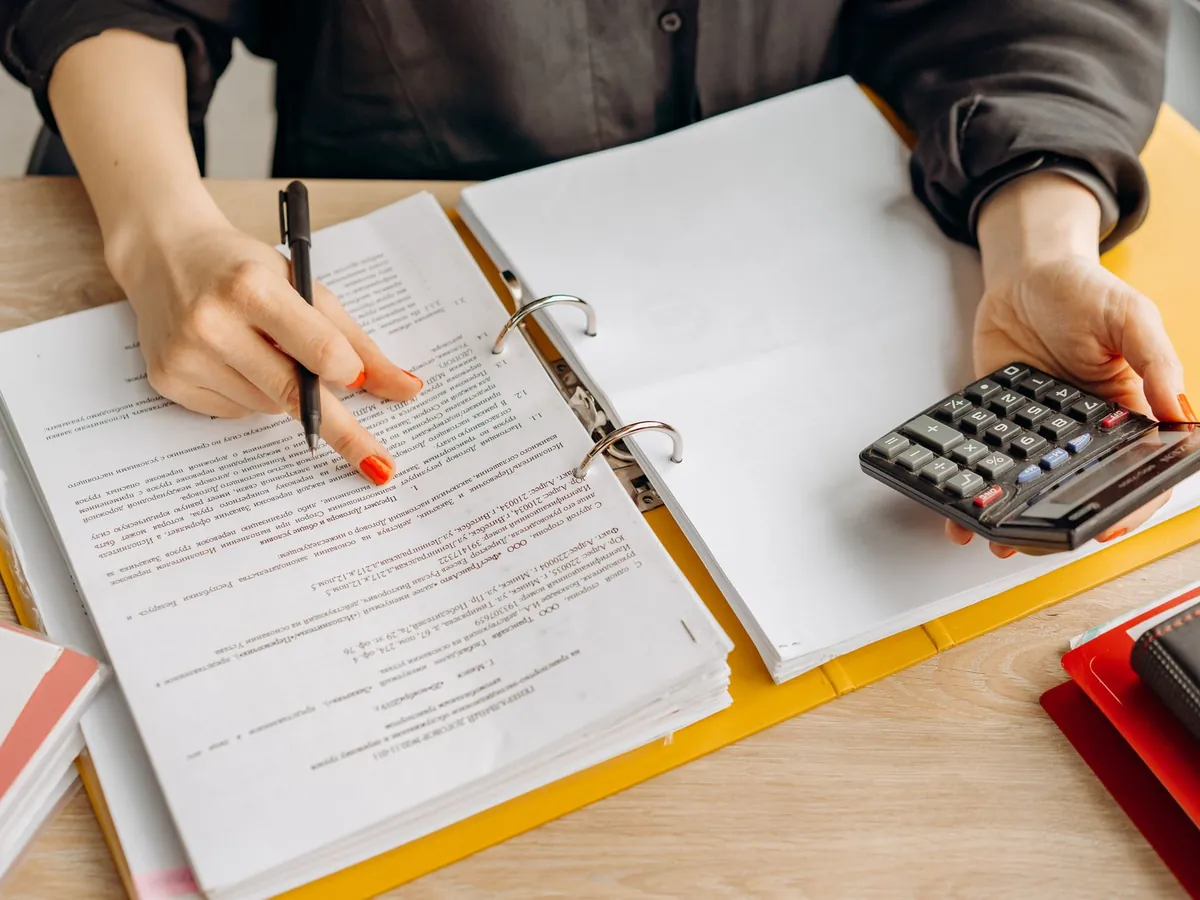Femme examinant des documents et utilisant une calculatrice sur une table en bois