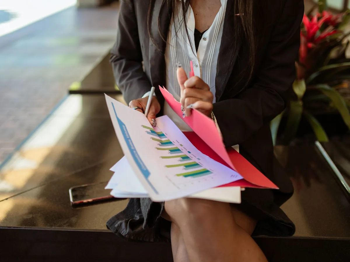 Femme en blazer assise en extérieur, consultant des documents de vente