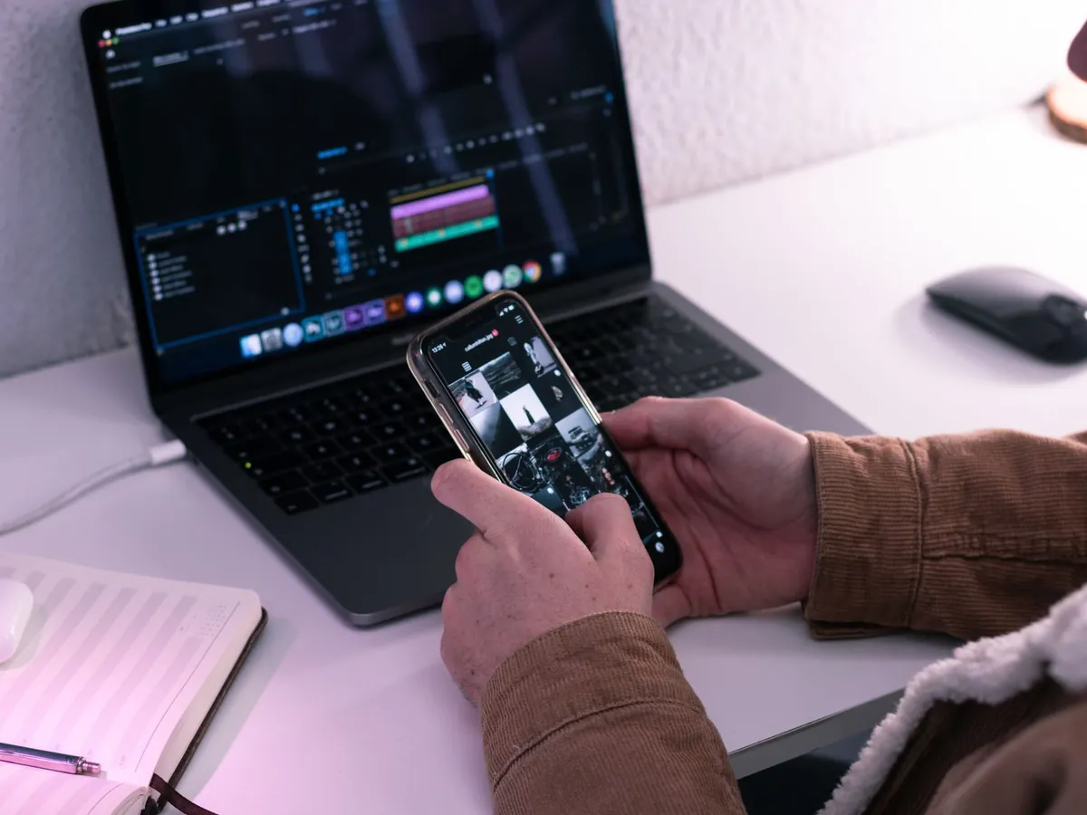 Homme assis à une table avec un netbook et un bloc-notes, regardant des photos sur son téléphone