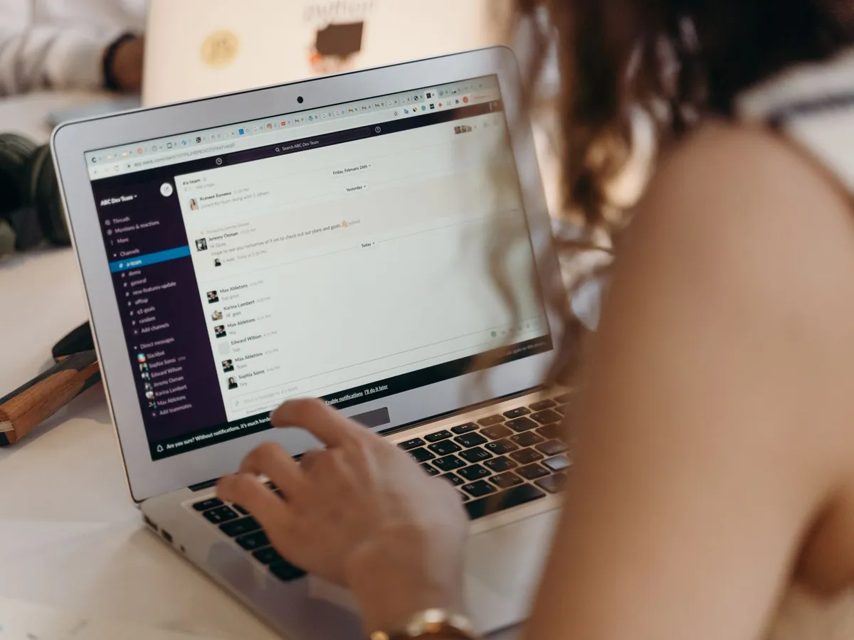 Femme d'affaires tapant sur son ordinateur portable au bureau, utilisant Slack pour la communication