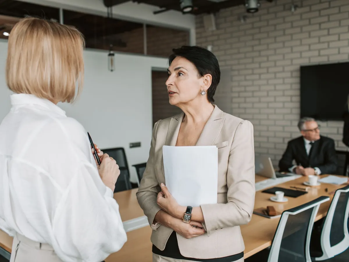 Deux femmes d'affaires en conversation lors d'une réunion professionnelle, dans un bureau moderne