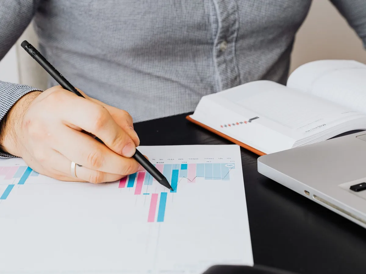 Analyste examinant un graphique sur papier, à côté d'un ordinateur portable et d'un carnet