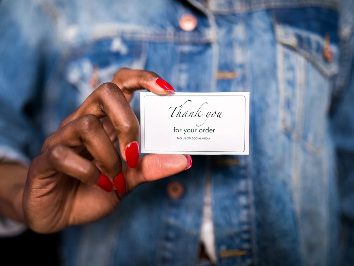 Femme en veste en jean tenant une carte « Thank You » avec des ongles rouges