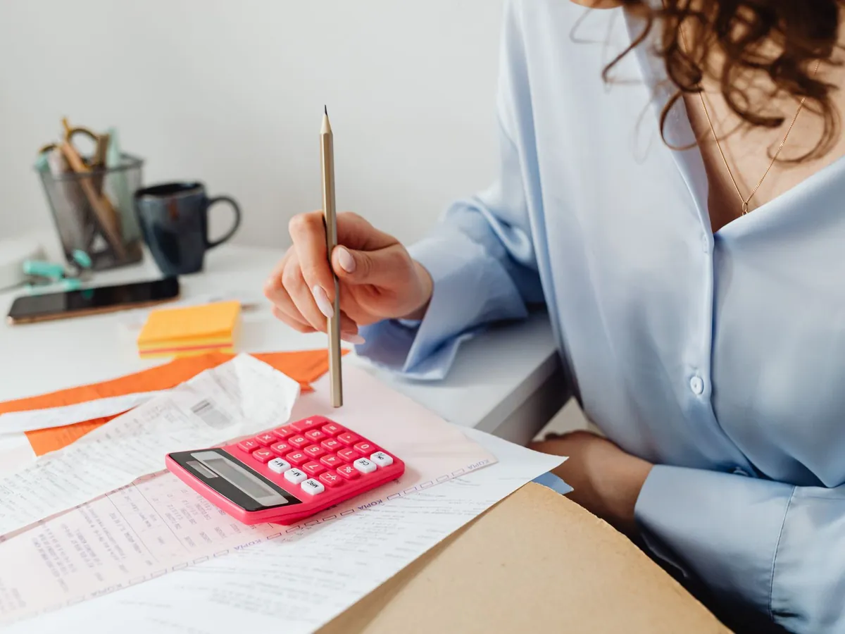 Femme calculant des dépenses à l'aide d'une calculatrice et de papiers sur son bureau