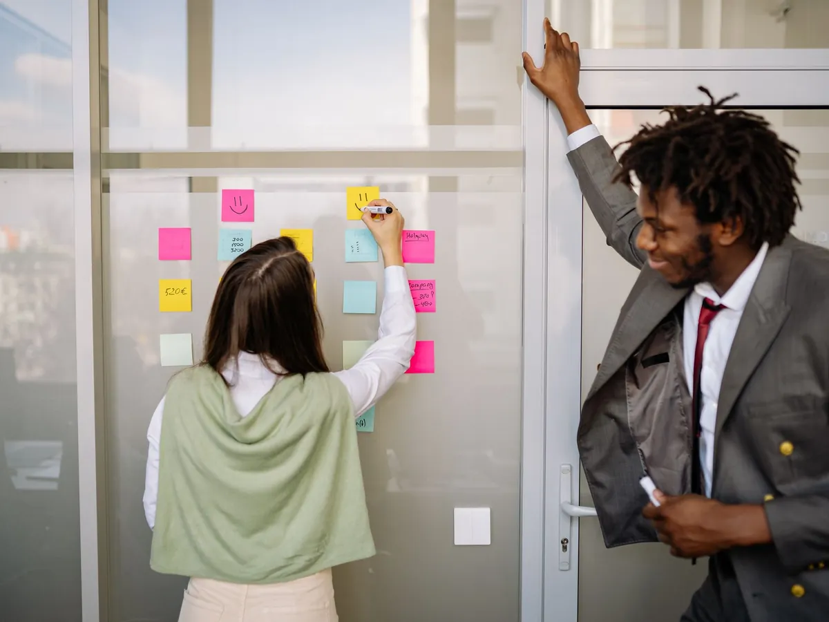 Deux professionnels réfléchissant avec des post-it sur une paroi vitrée dans un bureau moderne