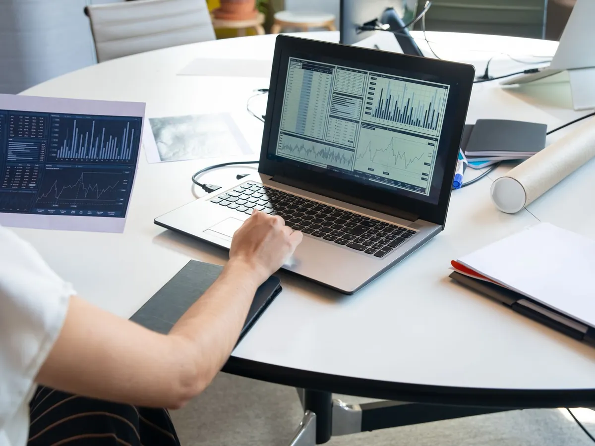 Professionnel analysant des graphiques financiers sur son ordinateur portable, dans un bureau moderne