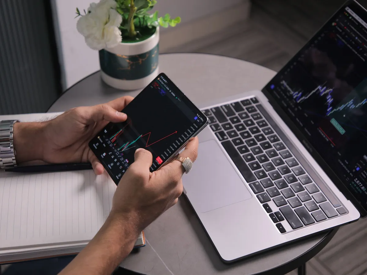 Homme analysant les tendances boursières sur ordinateur portable et application de trading mobile