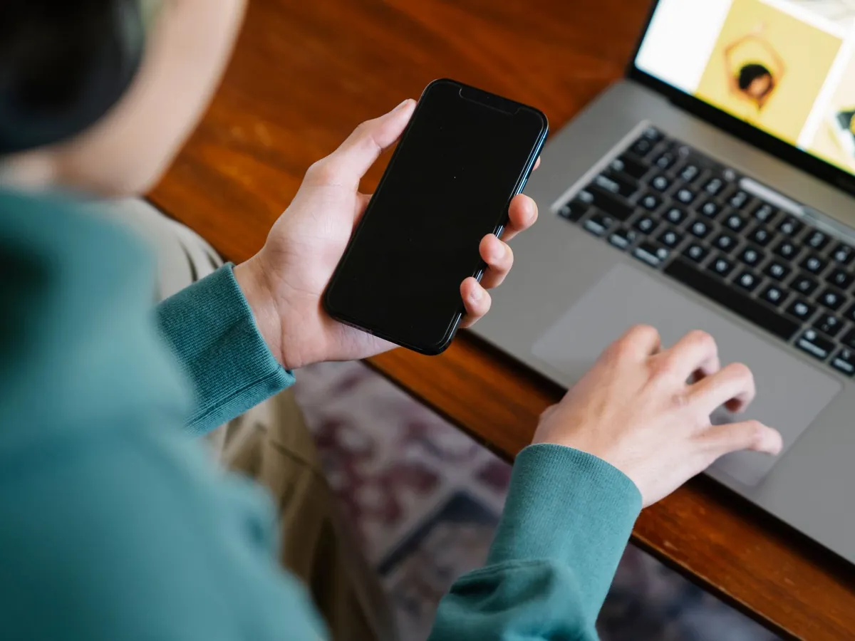 Gros plan d'une personne jonglant entre son smartphone et son ordinateur portable