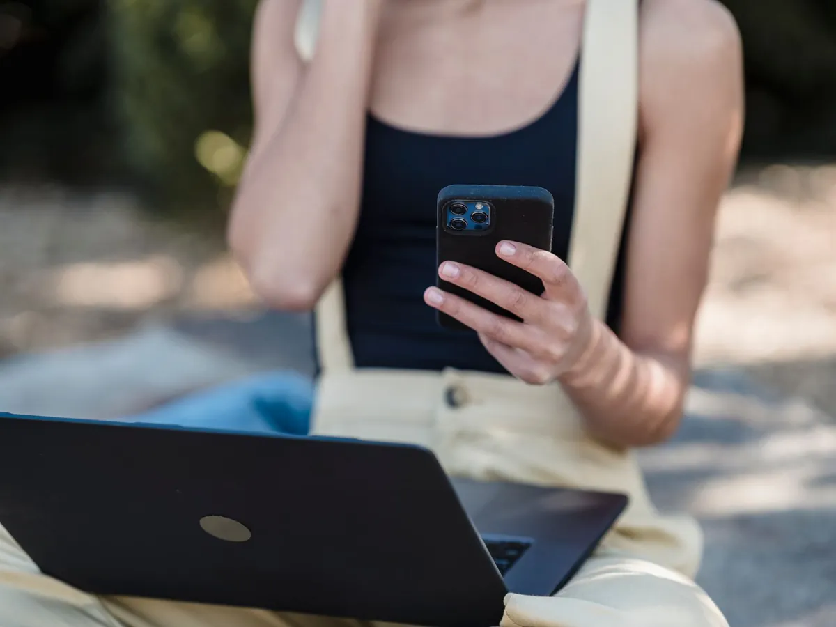 Femme anonyme aux épaules nues, assise en extérieur avec un ordinateur portable et un téléphone mobile