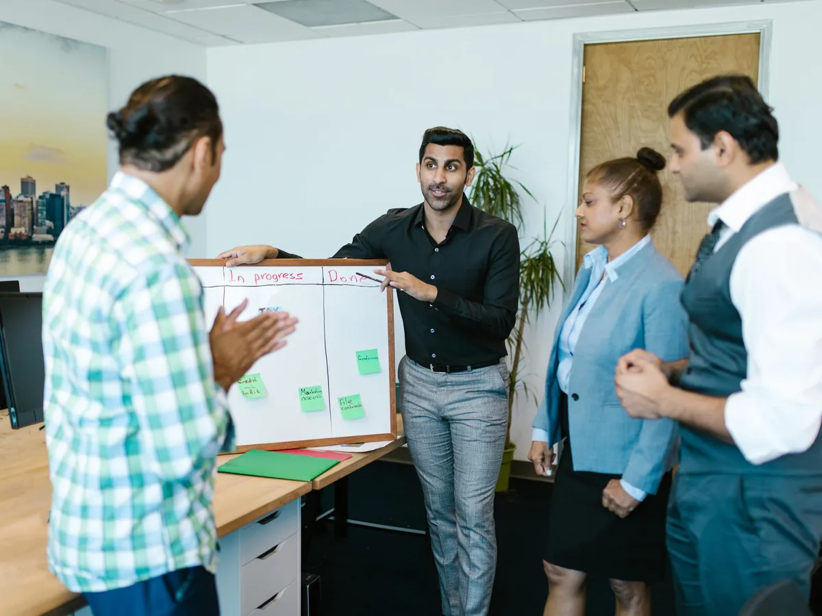 Équipe mixte échangeant sur l'avancement d'un projet devant un tableau, dans un bureau moderne