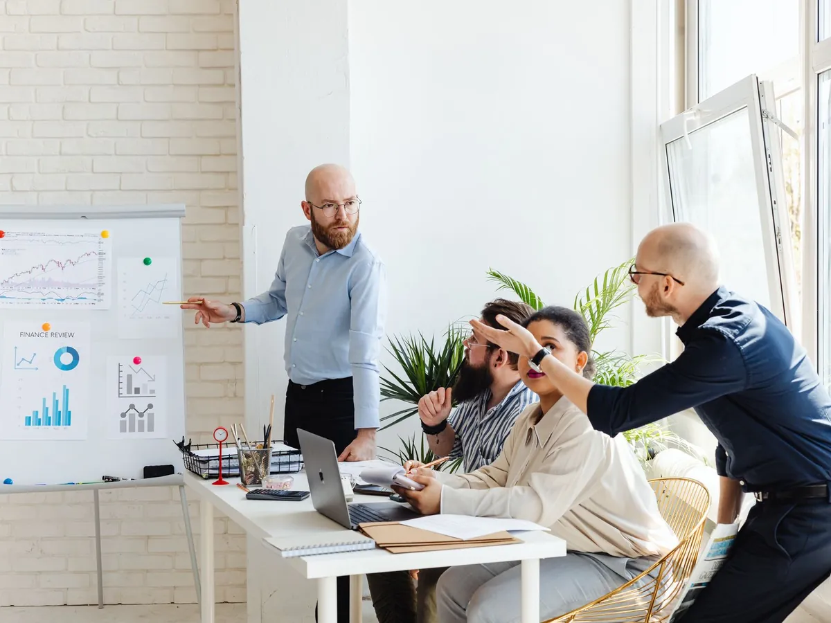 Groupe de professionnels en réunion d'affaires, discutant de graphiques financiers sur un tableau blanc