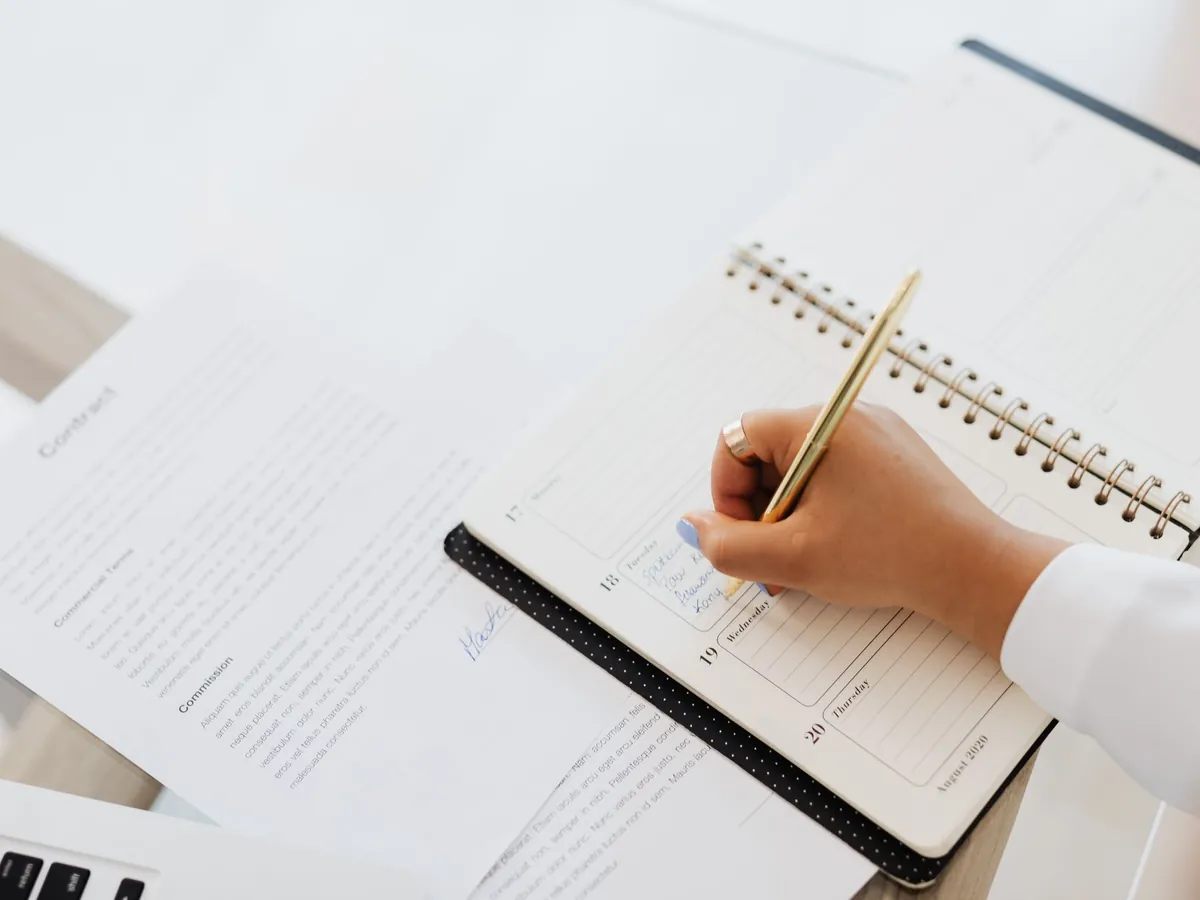 Gros plan d'une personne écrivant dans son agenda à côté d'un contrat posé sur le bureau
