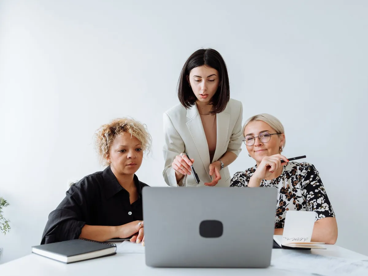 Trois femmes collaborant sur un projet devant un ordinateur portable, dans un bureau lumineux