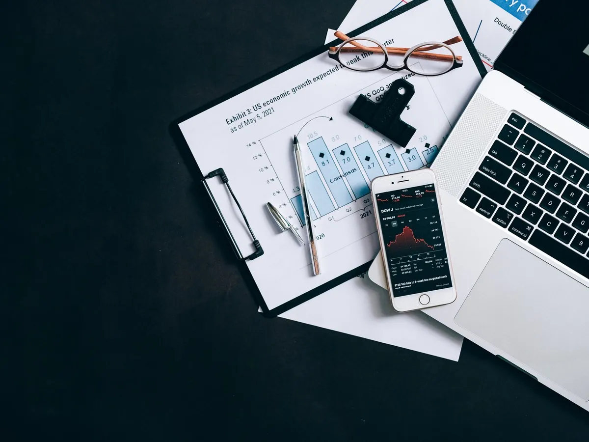Vue en plongée d'un bureau avec ordinateur portable, écritoire et smartphone affichant des cours boursiers