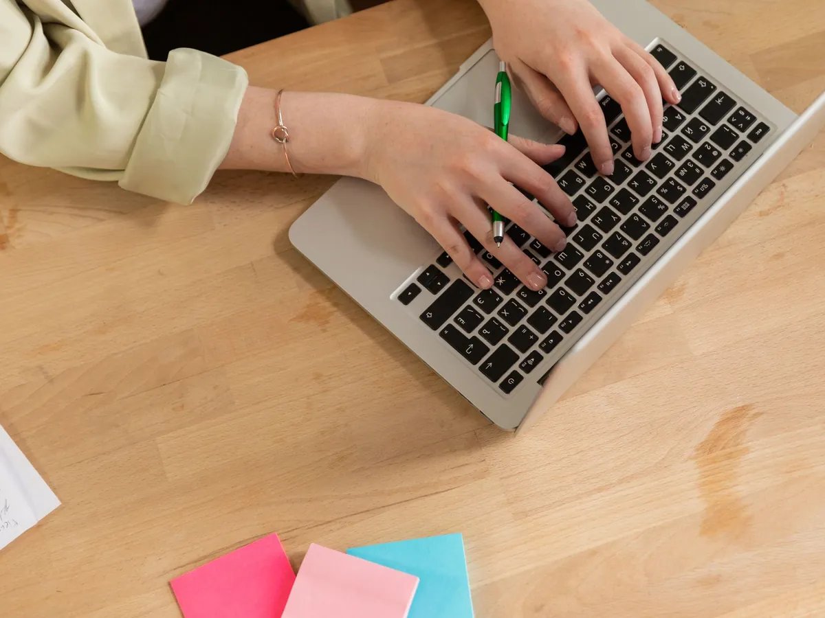 Mains tapant sur un ordinateur portable avec un stylo vert et des post-it colorés sur un bureau en bois