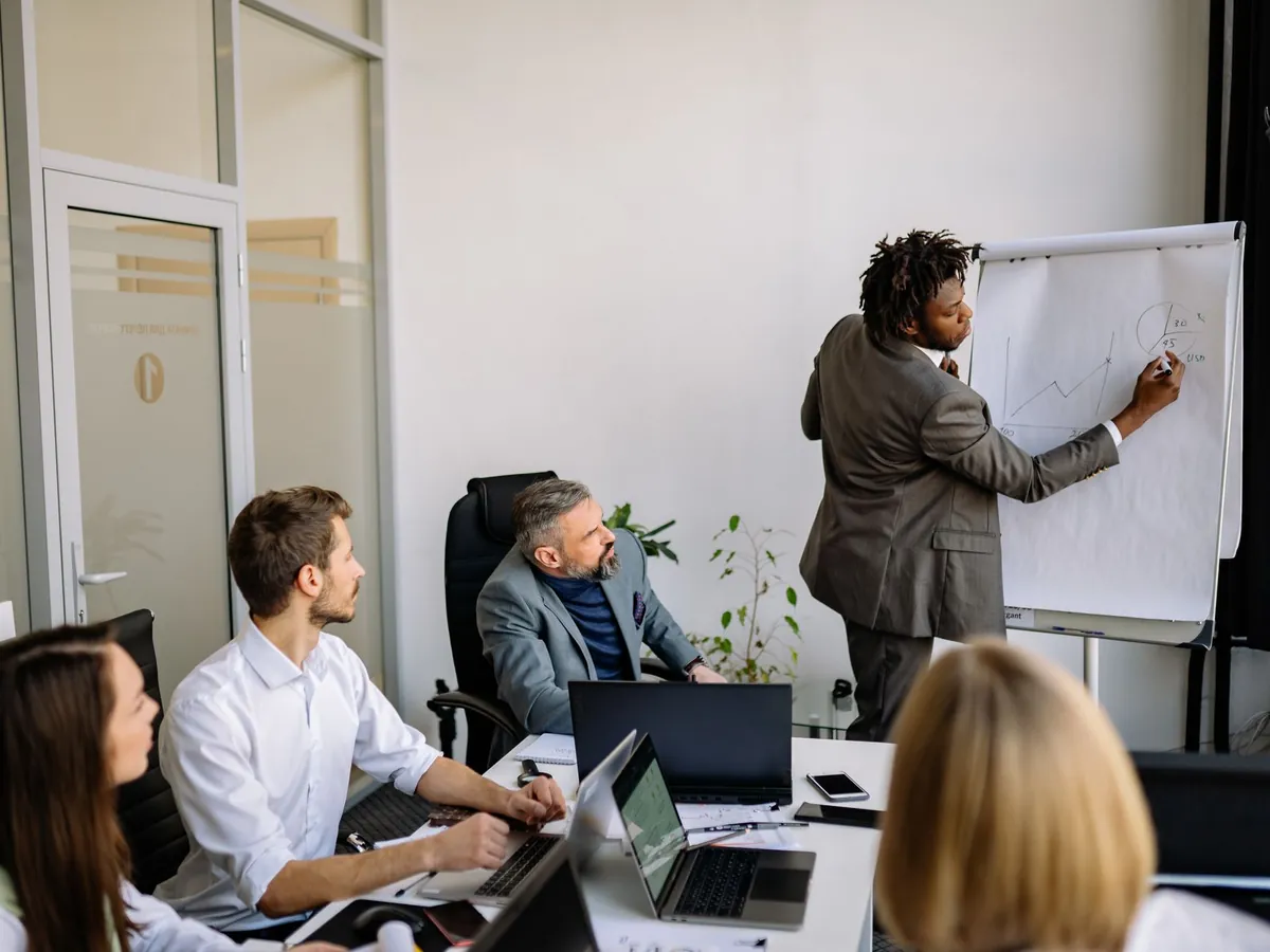 Équipe diversifiée en réunion stratégique, animée par un présentateur, dans un bureau moderne