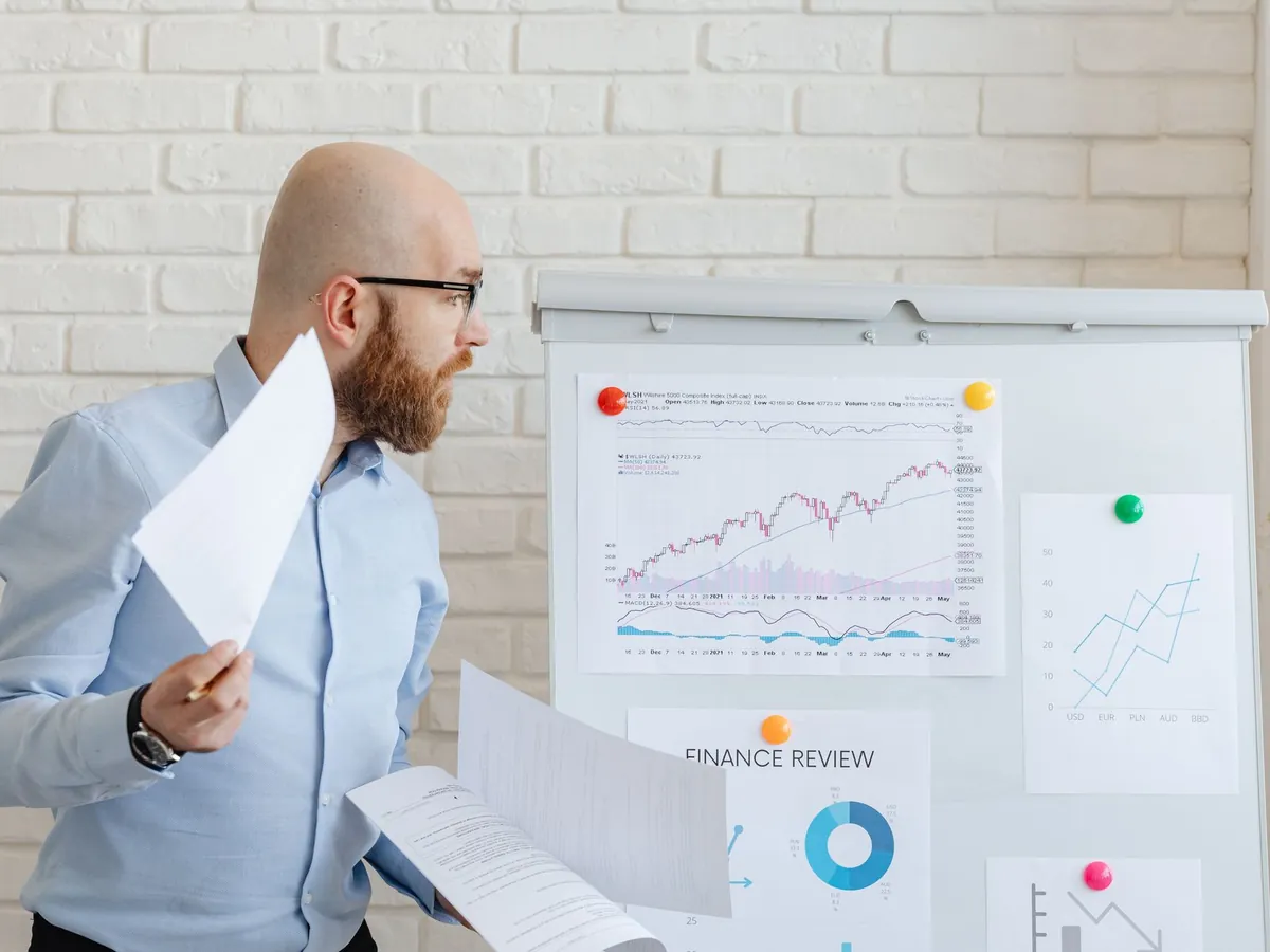 Homme d'affaires chauve en tenue casual chic analysant des graphiques financiers sur tableau blanc