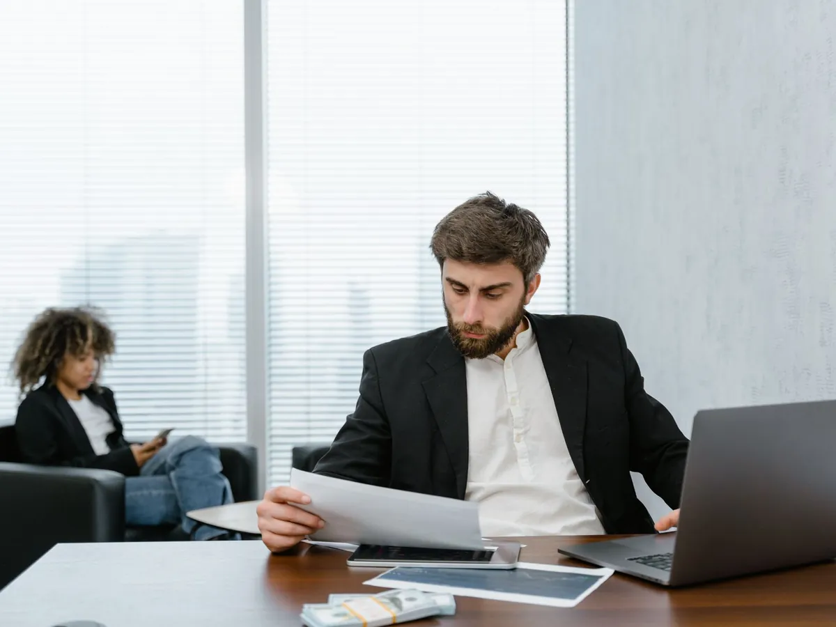Homme d'affaires concentré, examinant des rapports financiers à son bureau devant un ordinateur portable