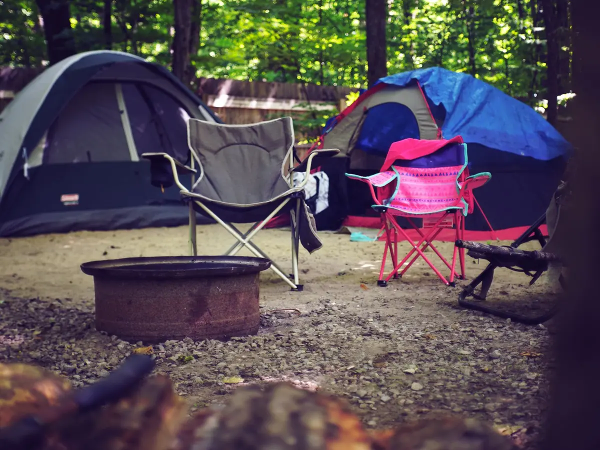 Campement paisible en forêt, avec tentes colorées, chaises de camping et foyer