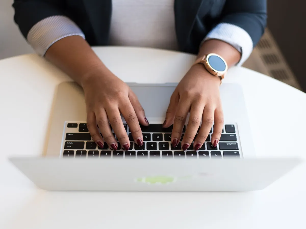 Mains de femme tapant sur un ordinateur portable sans fil, à un bureau moderne
