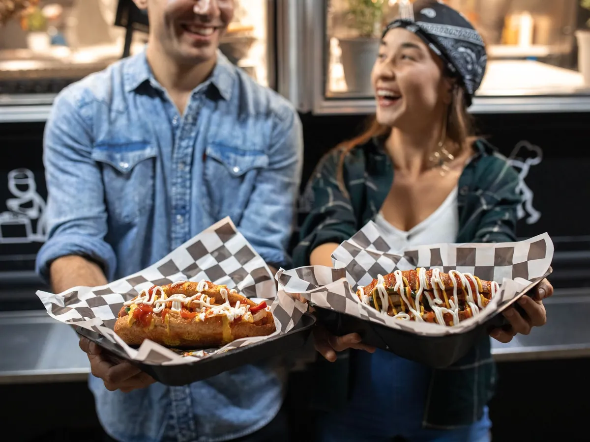Couple souriant tenant des street food gourmandes devant un food truck, de nuit
