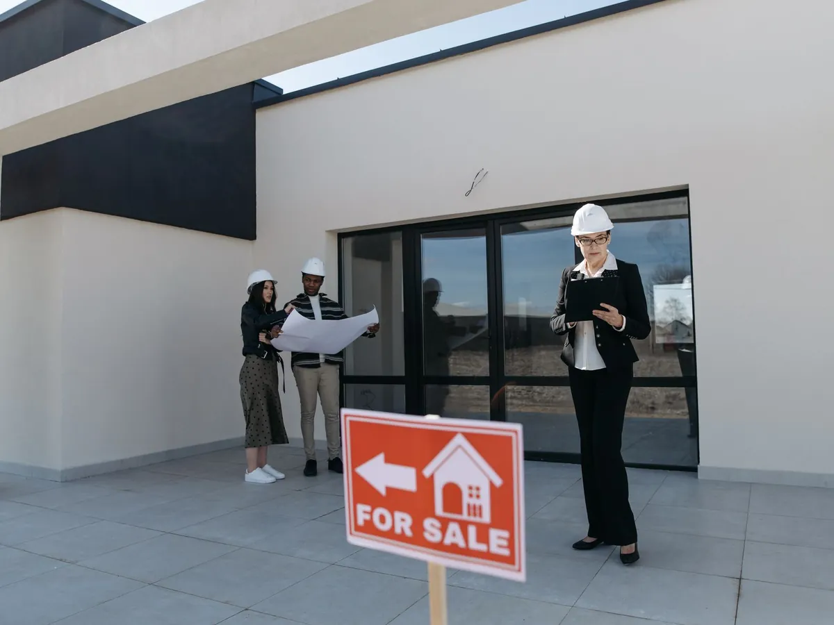 Agents immobiliers en casque de chantier examinant des plans à côté d'une maison à vendre
