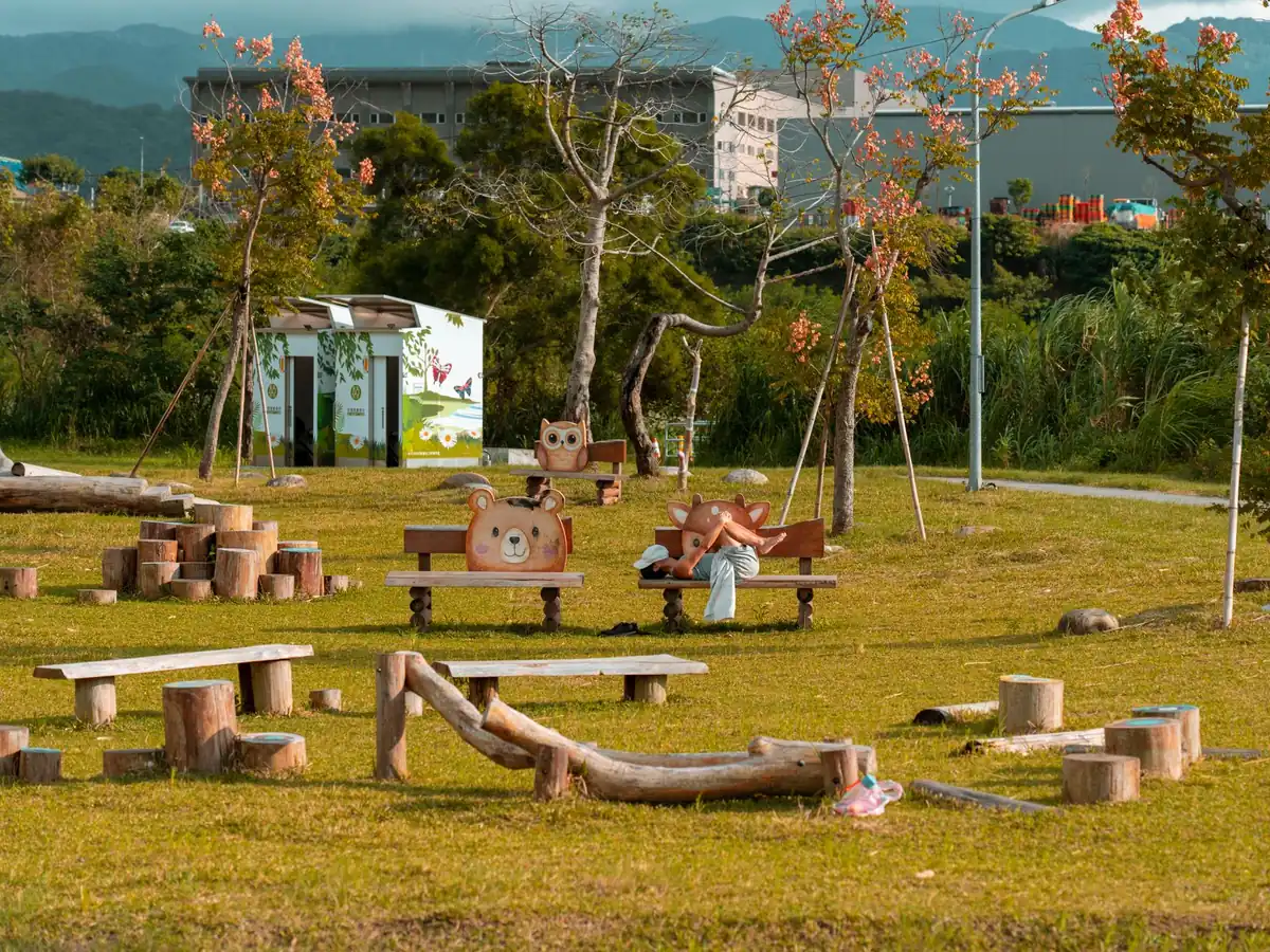 Parc urbain avec bancs en bois, pelouse verte, arbres et structures de jeux