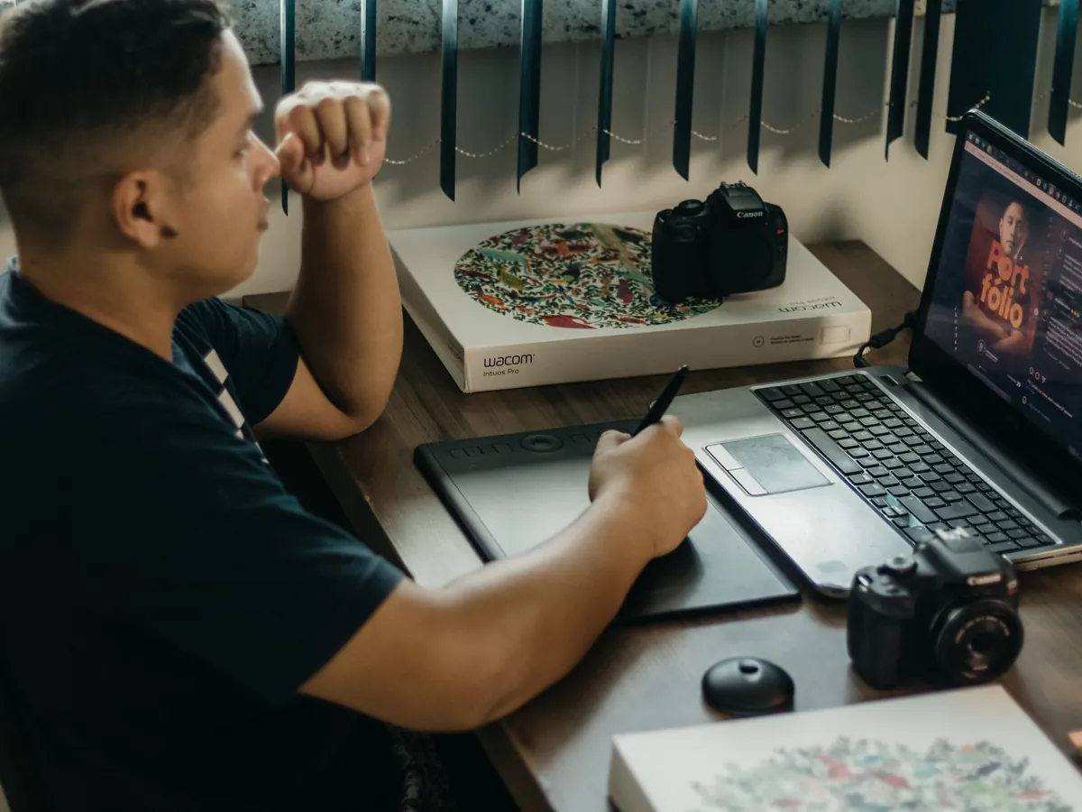Photographe retouchant ses images sur ordinateur portable et tablette Wacom, en intérieur