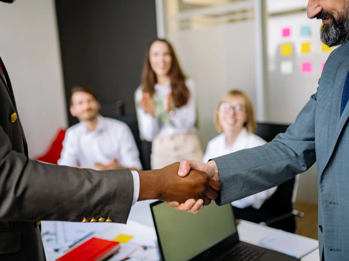 Poignée de main entre deux partenaires commerciaux devant une équipe réunie
