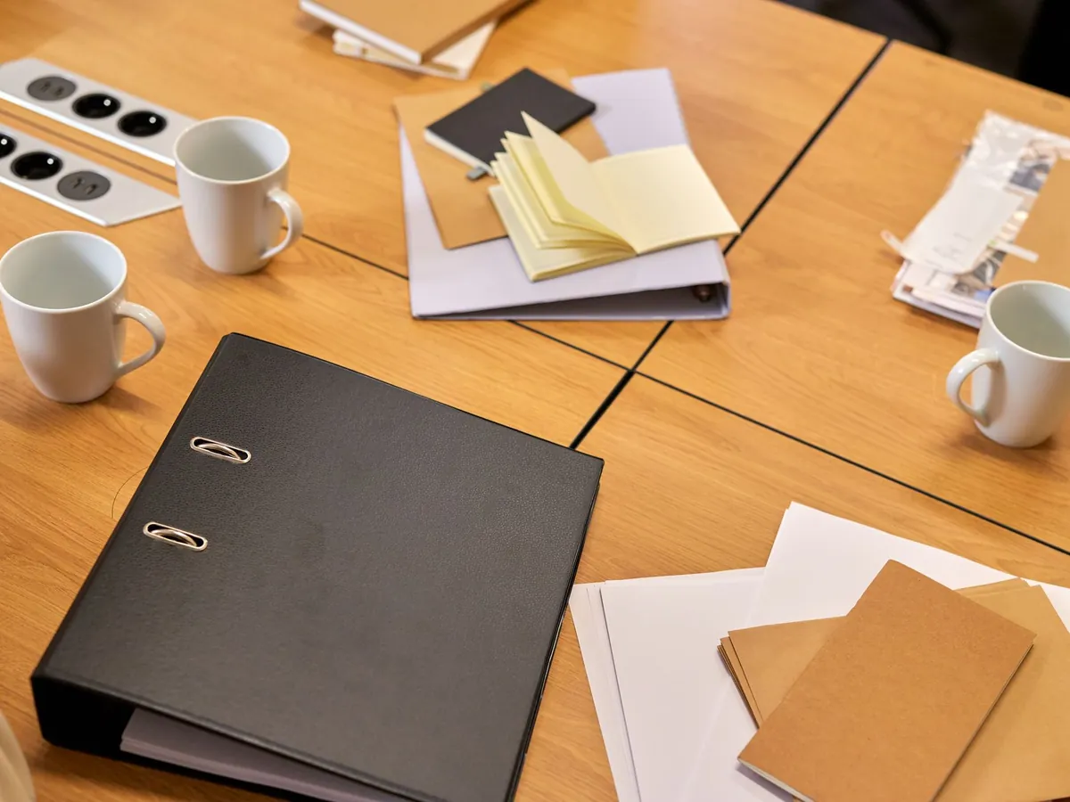 Classeur noir, carnets et tasses de café posés sur une table de travail en bois