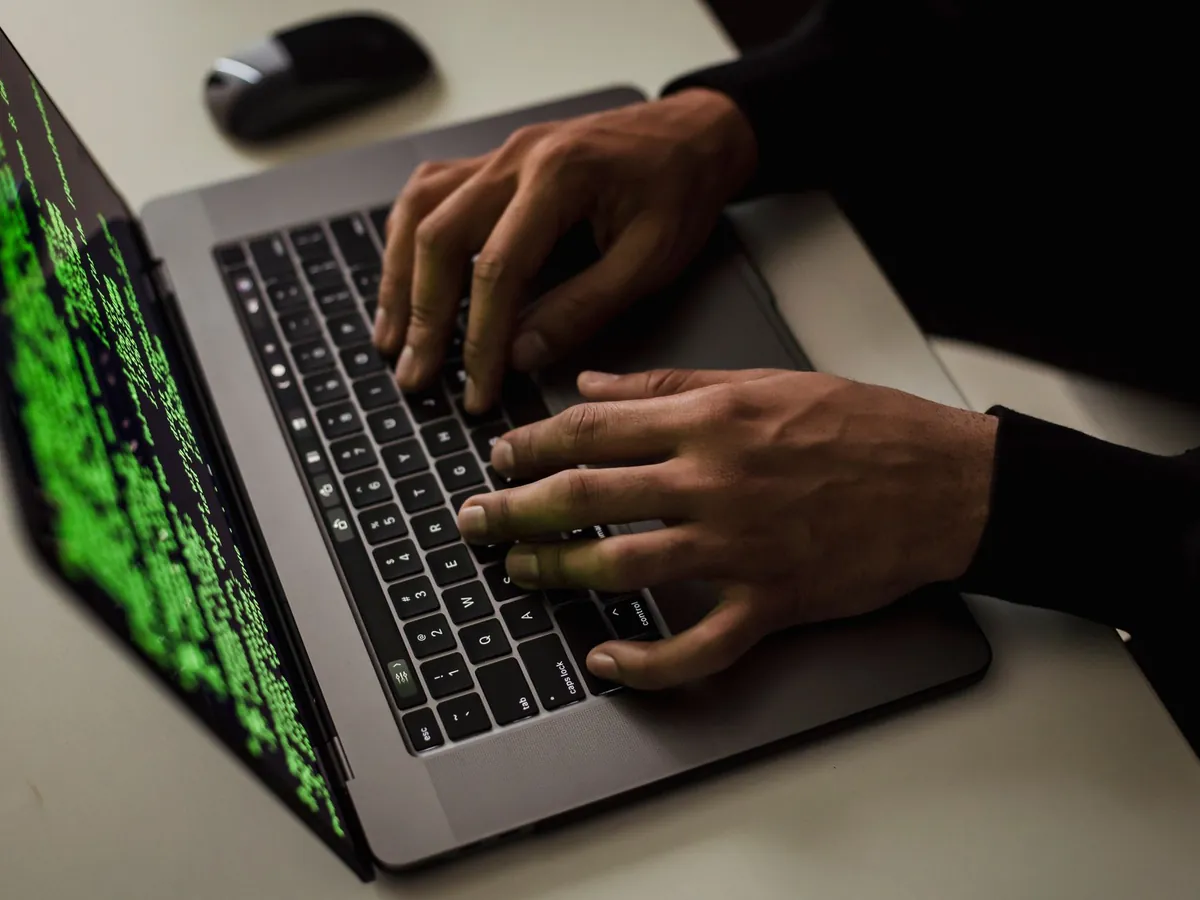 Mains d'un utilisateur sur le clavier d'un ordinateur portable, écran affichant du code