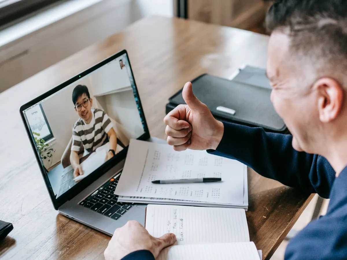 Formateur échangeant en visioconférence avec un participant, carnet et ordinateur portable devant lui