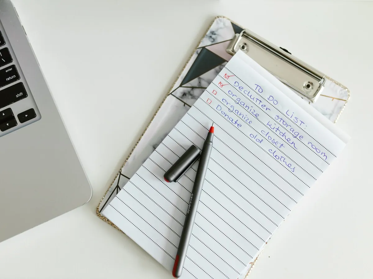 Liste de tâches bien organisée sur un presse-papiers, à côté d'un ordinateur portable et d'un stylo