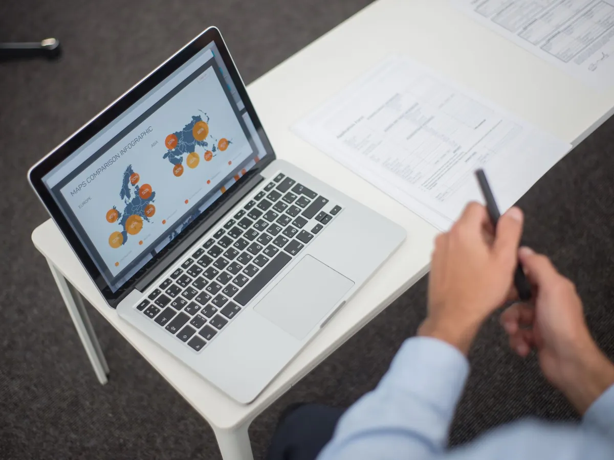 Professionnel analysant des infographies de données sur son ordinateur, documents et stylo à portée de main