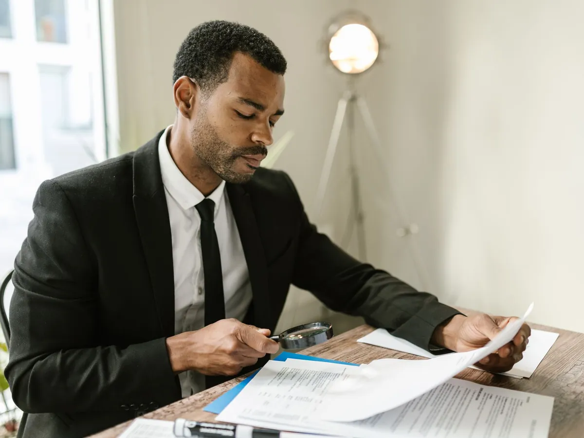 Homme examinant des documents à la loupe, à son bureau