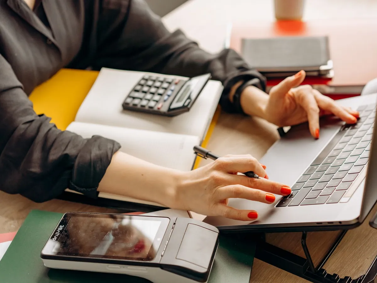 Personne utilisant un ordinateur portable avec un terminal de paiement et une calculatrice sur le bureau