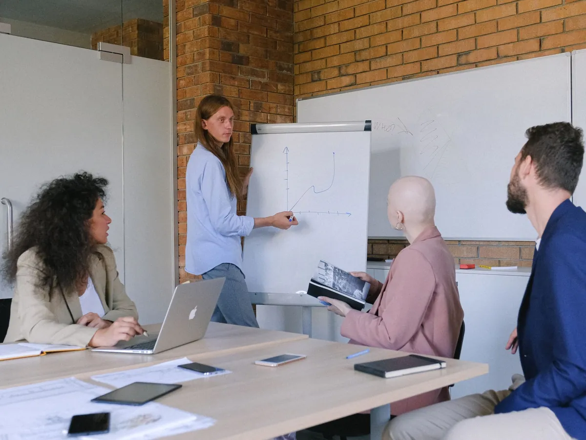 Collègues assis à une table, avec appareils et carnet, écoutant un intervenant qui dessine un graphique