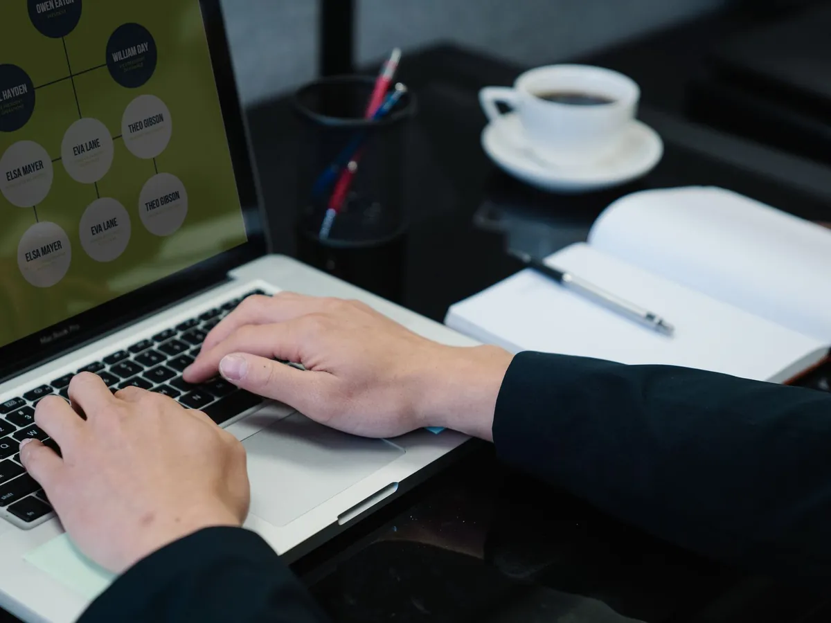 Mains tapant sur un ordinateur portable affichant un organigramme, avec un carnet et un café à côté