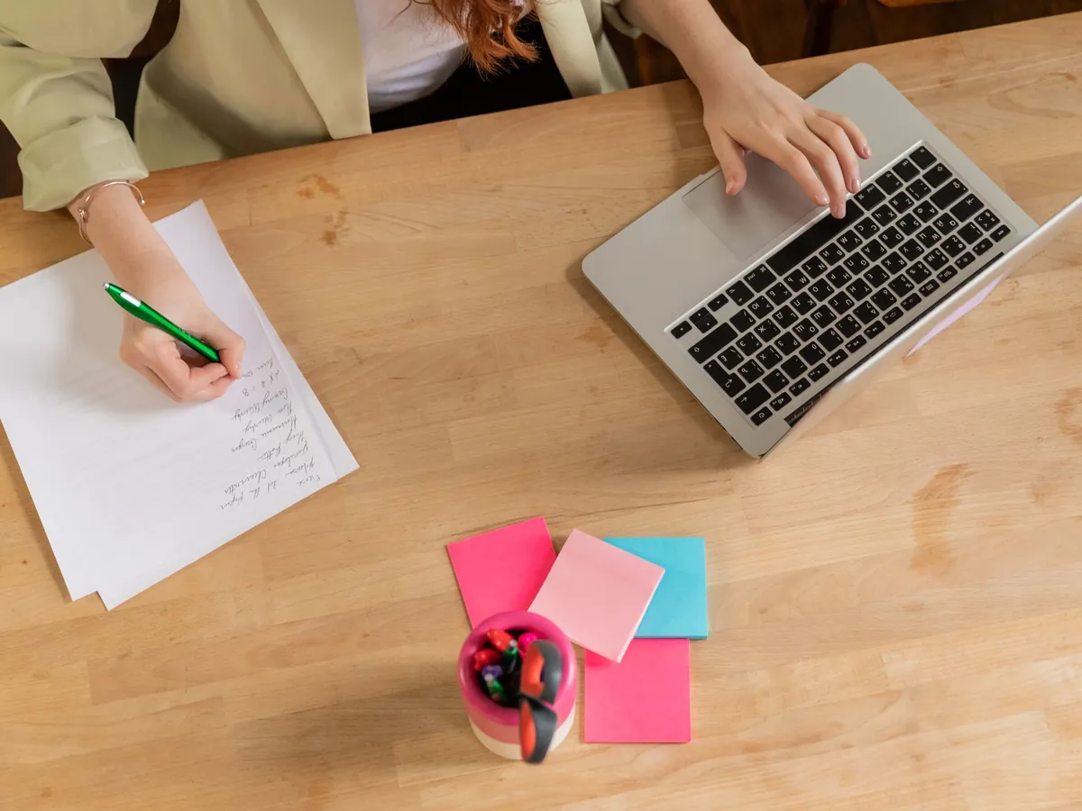 Vue de dessus d'une personne prenant des notes et tapant sur son ordinateur, bureau en bois