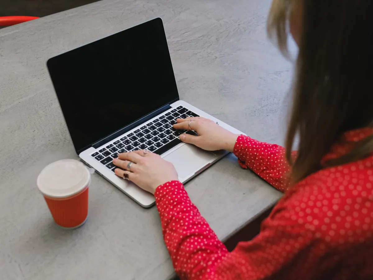 Femme en chemisier à pois rouges tapant sur un ordinateur portable sur une table grise avec une tasse de café