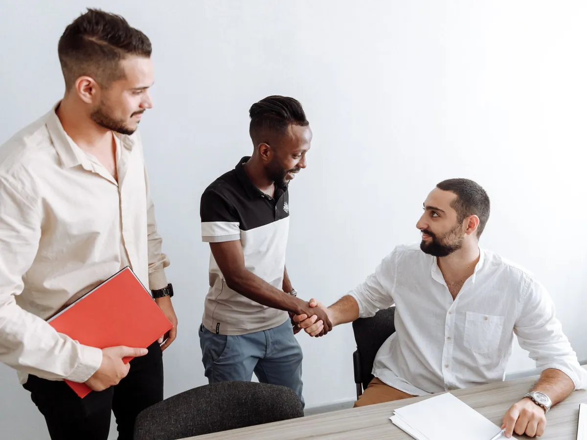 Trois hommes au bureau, se serrant la main, dans un esprit d'équipe et de diversité