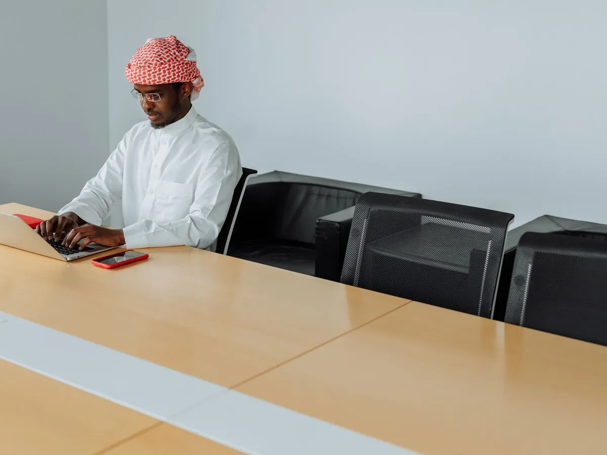 Homme en tenue traditionnelle travaillant sur son ordinateur portable dans un bureau moderne