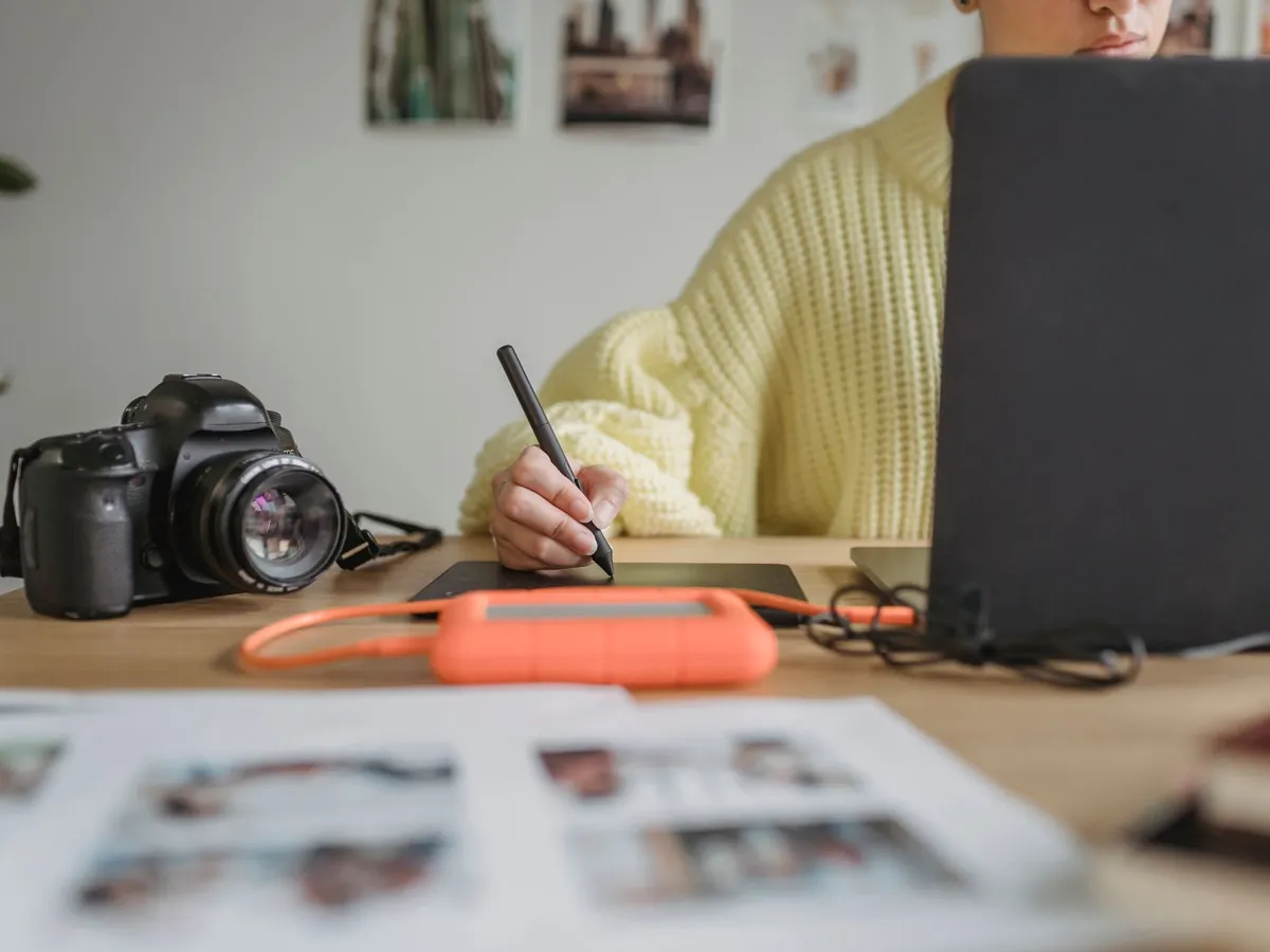 Femme anonyme retouchant des photos sur un netbook avec une tablette graphique, appareil photo à proximité