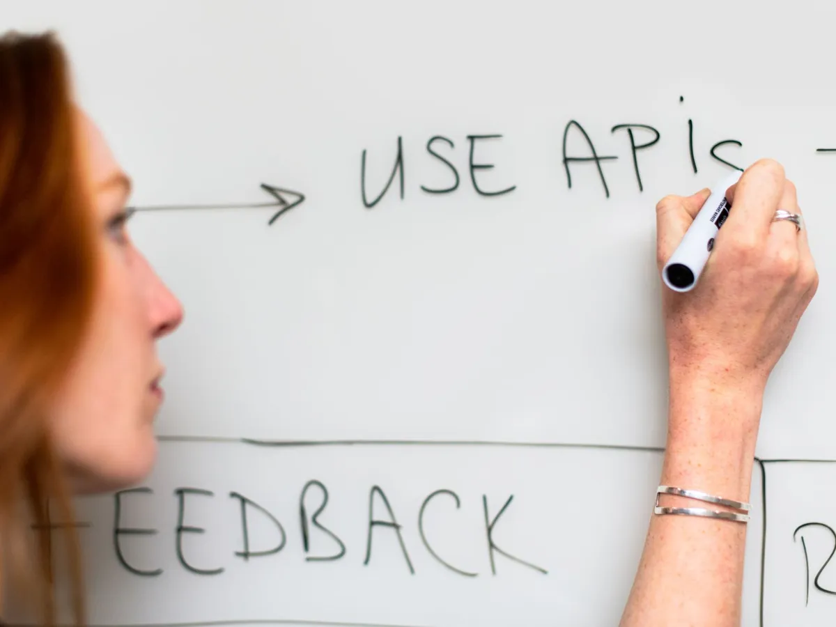 Femme écrivant « Use APIs » sur un tableau blanc, lors d'une réflexion sur la planification logicielle