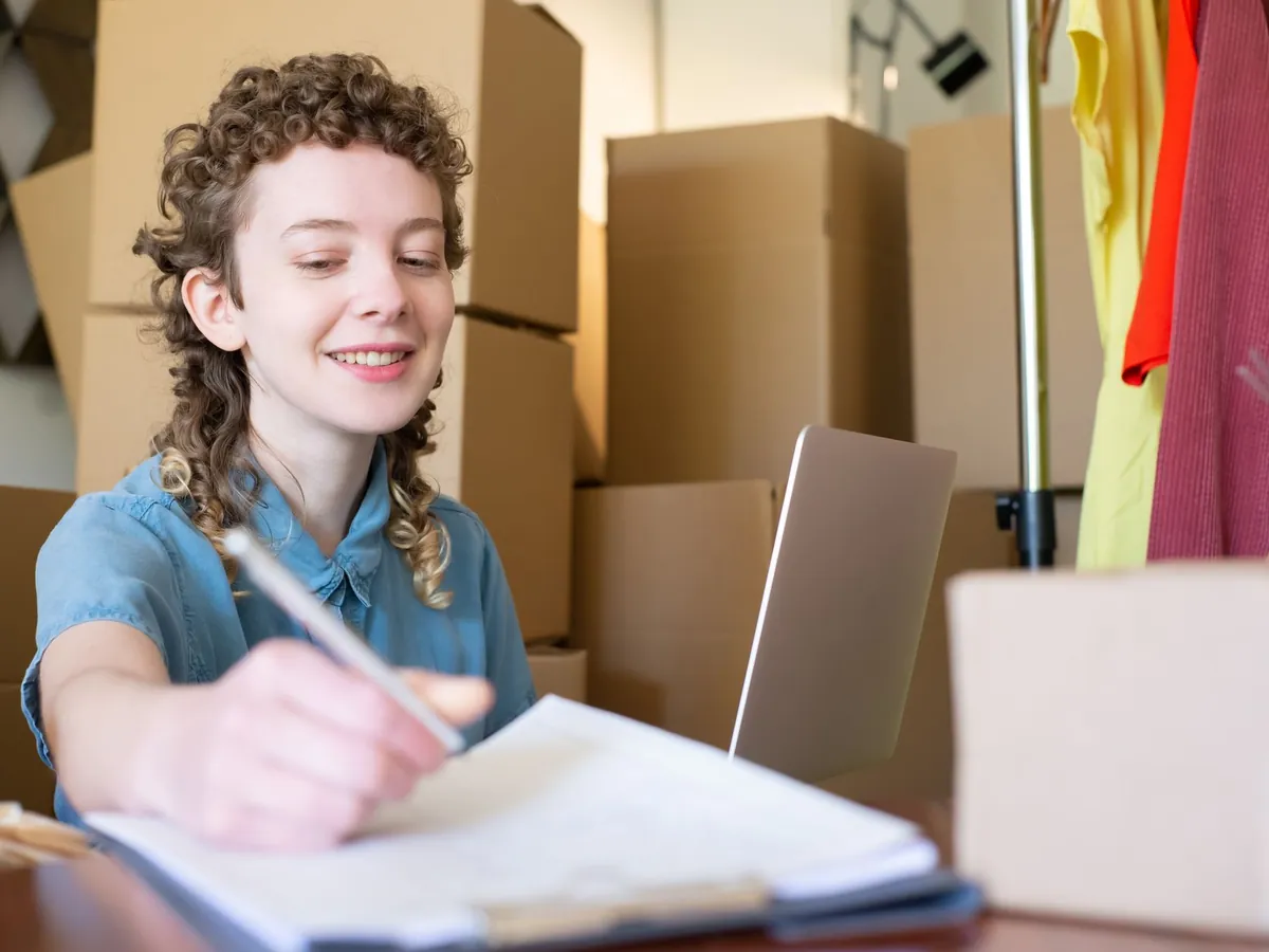 Jeune femme souriante gérant sa petite entreprise, ordinateur portable et colis autour d'elle