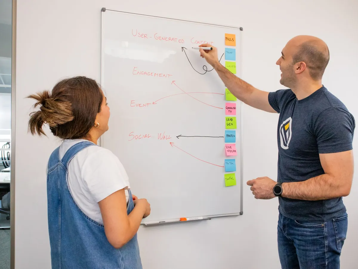Deux collègues font un brainstorming marketing devant un tableau blanc, dans un bureau moderne