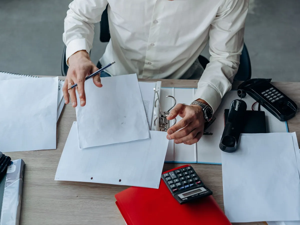 Professionnel organisant des documents sur un bureau encombré, axé sur la productivité
