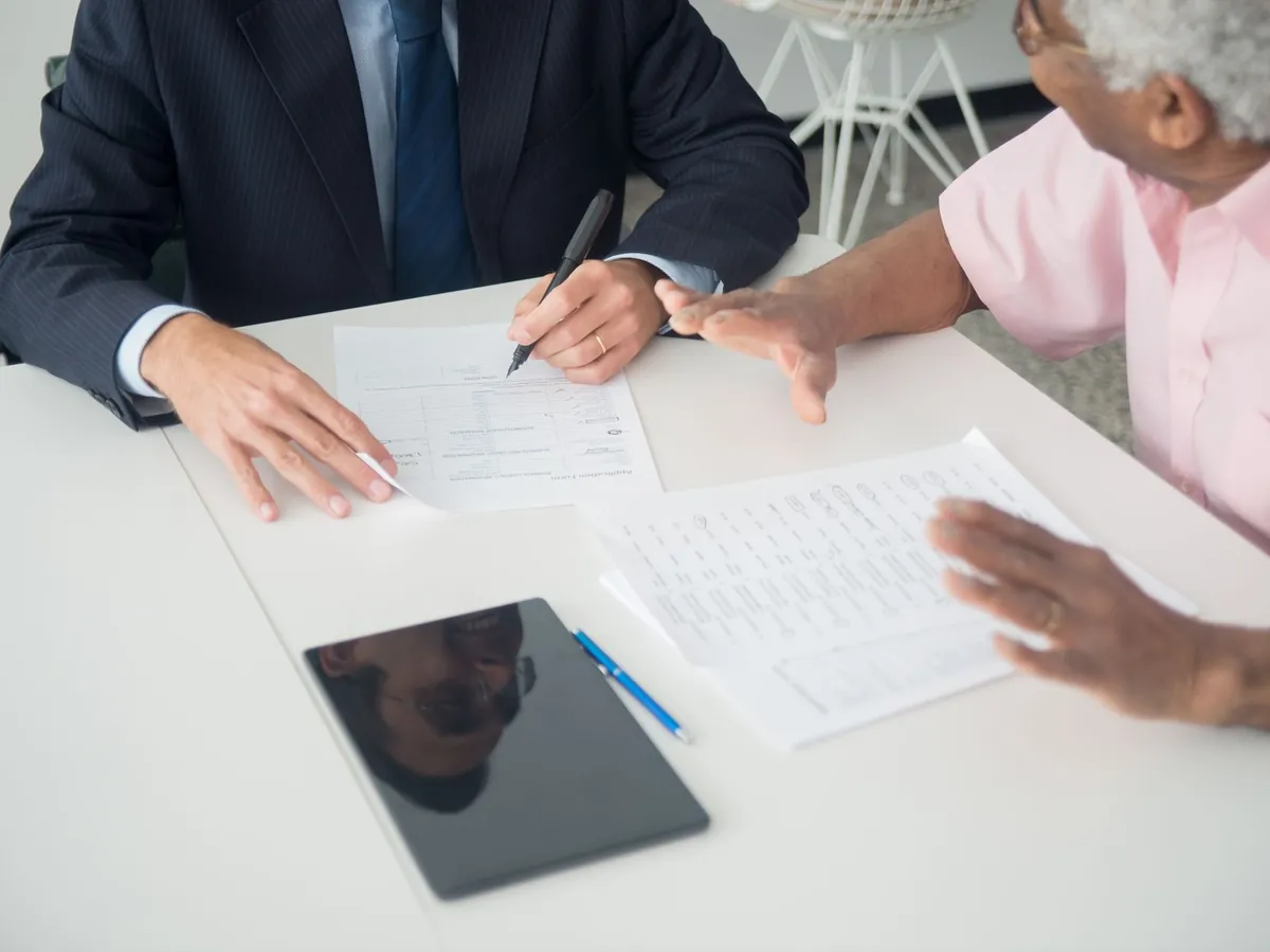 Réunion d'affaires entre une cliente âgée et un consultant examinant des documents à une table de bureau
