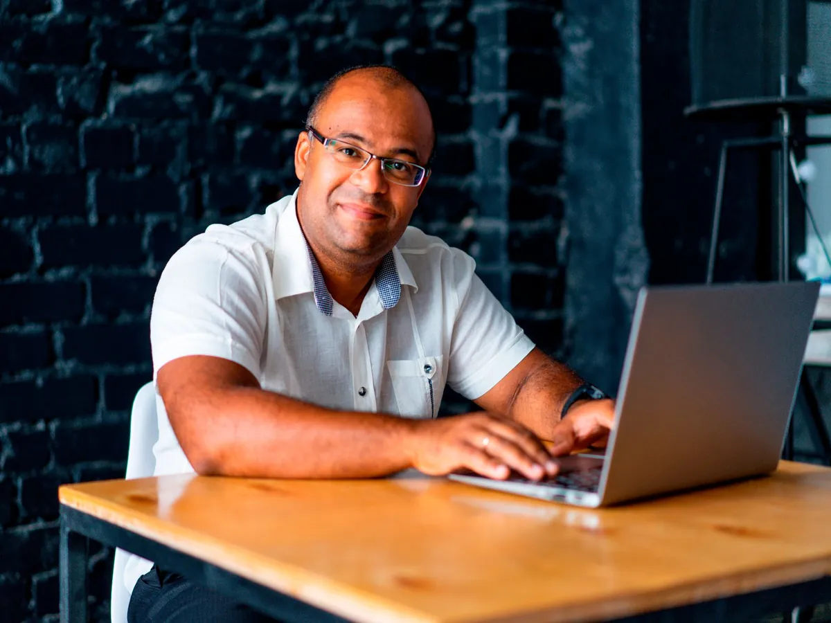 Homme adulte souriant, assis à son bureau devant un ordinateur portable, dans un bureau moderne